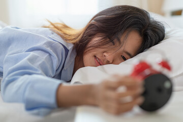 Asian woman is waking up and watching her alarm clock in the morning