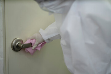 Worker in protective suit wiping door handle with disinfectant	
