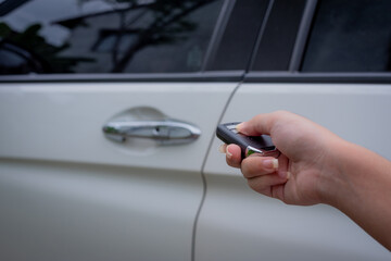 Female hand holding and pushing car remote control to lock or unlock the car.