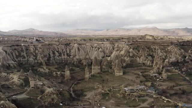 Aerial of surreal natural features of mountains on cloudy sky background. Action. Rare houses built near the picturesque rock formations. 