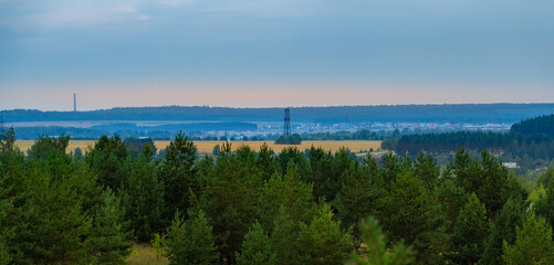 Fototapeta na wymiar A high-voltage line in the field and the city of Mariinsky Posad in the distance, behind the field, in the evening, a fir forest in the foreground.