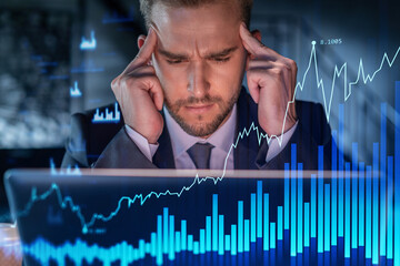 Handsome businessman in suit at workplace working with laptop to optimize trading strategy at...