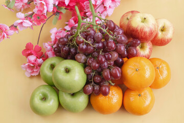 Grapes,Oranges and Apples put at the right side of blurred pink flowers,