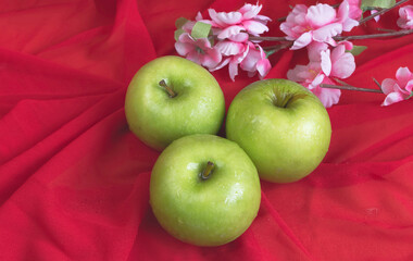 Three Green Apples put in front of blurred pink flowers