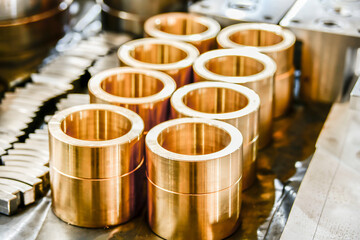 Bronze bushings for plunger hydraulic pumps, made on a cnc lathe, stand on a rack in a warehouse.