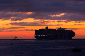 A container ship leaves harbour just as the sun rises over the horizon.