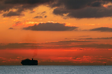 A large container ship leaves harbor from Malta Freeport just as the sun rises over the horizon.