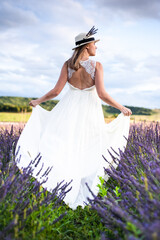 Fototapeta premium Beautiful bride in wedding dress and hat on the lavender field