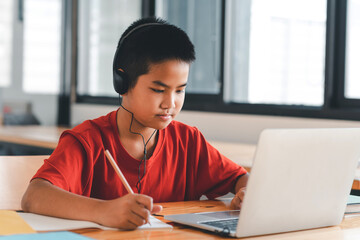 Image of a man student studying online wearing headphones to taking notes in his room using a laptop.