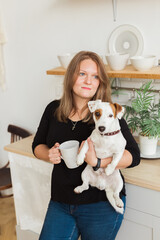 Happy female owner of jack russell terrier dog, feels responsibility of caring about pet, standing against kitchen background. People and relationship with animals