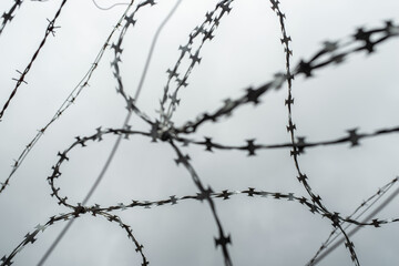 Fototapeta na wymiar Out of focus photo of barbed wire against a grey cloudy sky. The heart shape in barbed wire.