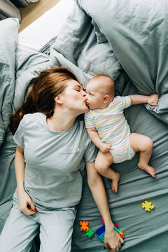 Vertical image of mom kissing her little infant daughter lying on gray bedding.
