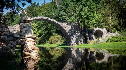 Papier Peint photo autocollant Le Rakotzbrücke Teilansicht der Rakotzbrücke mit davor stehender Steinsäule und Spiegelung im See
