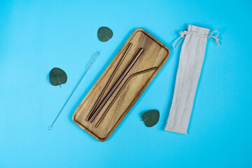 A set of metal straws on a wooden plate with leaves around it and a bag