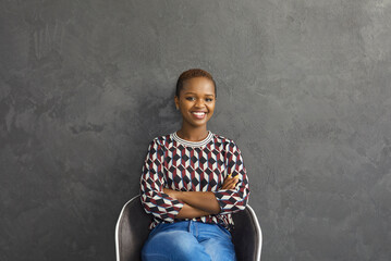 Portrait of an attractive young dark-skinned woman sitting on a chair and smiling sincerely....