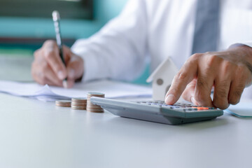 Close-up of a man in white using a calculator and taking notes accounting report concept of costing and saving money for building a solid foundation in the future. - obrazy, fototapety, plakaty