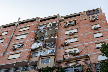 Old building, with a brick facade, some balconies with hanging clothes and several air conditioners in the windows. 