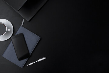 top view of office workspace Black table with notebook, keyboard, phone, notepad, pen and a cup of...