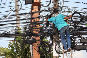 An electrician is climbing an electric pole to inspect and install wires without wearing protective...