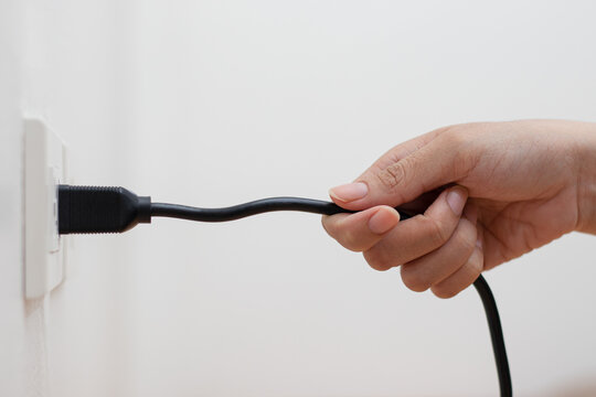 A woman's hand is pulling the power cord in a wrong design. Risk of danger and damage to the power plug, power cord.