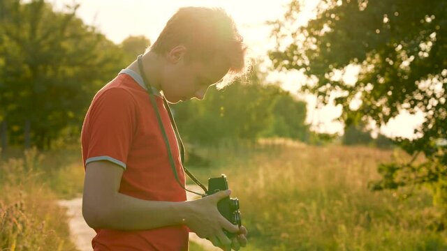 4k stock video footage of young handsome teenage kid using old vintage analog photo or video camera outdoors on sunset sunny summer time