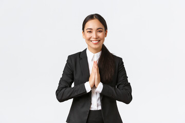Hopeful glad asian businesswoman in black suit bowing politely and say namaste, greeting clients and smiling friendly. Thankful female manager thanking for help, being grateful, appreciate help - obrazy, fototapety, plakaty