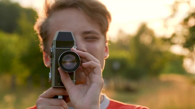 Close-up 4k stock video footage of portrait of young handsome white blonde teenage kid using old vintage analog video camera outdoors on sunset sunny summer time