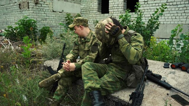 two soldiers sit tired among the ruins and talk