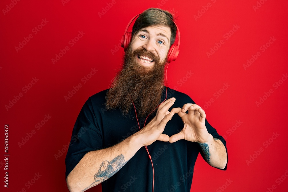 Sticker Redhead man with long beard listening to music using headphones smiling in love doing heart symbol shape with hands. romantic concept.