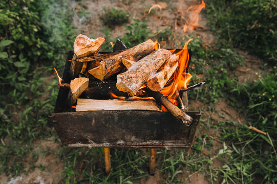 Burning pine firewood lies in a rusty metal grill. Bonfire in nature.