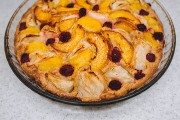 Delicious, fresh, baked apple, peach, raspberry pie close-up in a round glass form.