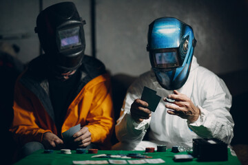 Two welders in welding masks play poker