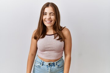Young brunette woman standing over isolated background winking looking at the camera with sexy expression, cheerful and happy face.