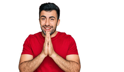 Fototapeta na wymiar Hispanic man with beard wearing casual red t shirt praying with hands together asking for forgiveness smiling confident.