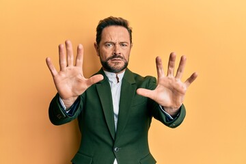 Middle age man wearing business suit afraid and terrified with fear expression stop gesture with hands, shouting in shock. panic concept.