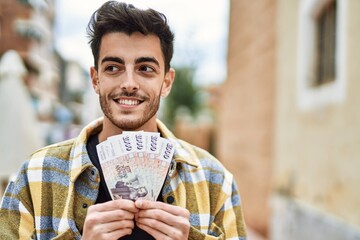 Handsome hispanic man smiling happy and confident at the city holding 1000 iceland krona banknotes