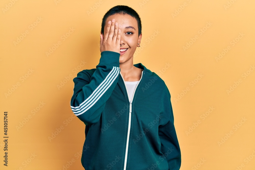 Sticker beautiful hispanic woman with short hair wearing sporty jacket covering one eye with hand, confident