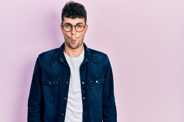 Young hispanic man wearing casual clothes and glasses making fish face with lips, crazy and comical gesture. funny expression.