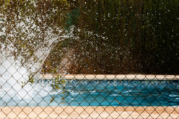 Splash of water in a lonely pool through a fence. Shock concept, summer and solitude