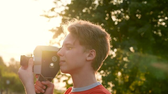 Close-up 4k stock video footage of young handsome teenage kid using old vintage analog video camera outdoors on sunset sunny summer time