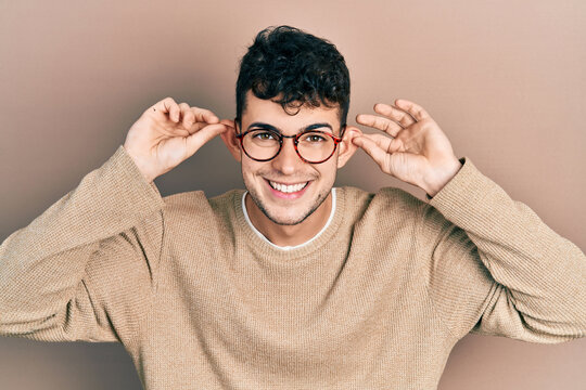 Young hispanic man wearing casual clothes and glasses smiling pulling ears with fingers, funny gesture. audition problem