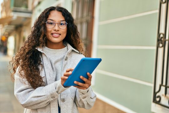 Young latin woman smiling happy using touchpad at the city.