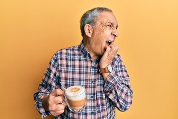 Handsome senior man with grey hair drinking a cup coffee looking stressed and nervous with hands on mouth biting nails. anxiety problem.