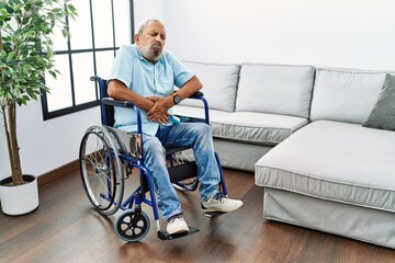 Handsome senior man sitting on wheelchair at the living room with hand on stomach because nausea, painful disease feeling unwell. ache concept.