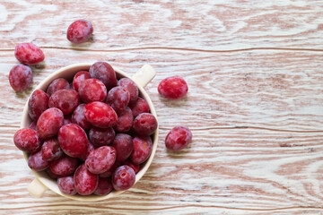 Plum. Harvest. Fresh red plum in a bowl on a light wooden surface with space for text, top view, shallow depth of sharpness
