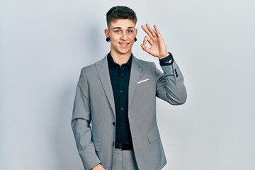 Young caucasian boy with ears dilation wearing business jacket smiling positive doing ok sign with hand and fingers. successful expression.