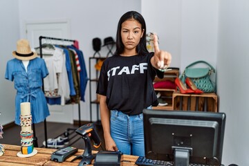 Young hispanic woman working as staff at retail boutique pointing with finger up and angry expression, showing no gesture