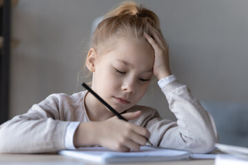 Unhappy small kid sit at desk at home handwrite in notebook lack motivation prepare homework for school. Sad little girl child feel lazy unmotivated doing task assignment. Education concept.