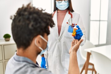 Young latin doctor woman giving bottle of pills to man at medical room.