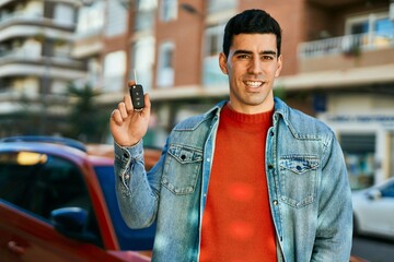 Young hispanic man smiling happy holding key car at the city.